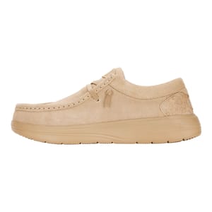A beige suede shoe with a moccasin-style design, featuring a rounded toe, minimal lacing, and a thick sole for cushioning.