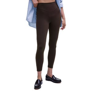 A person wears high-waisted dark brown leggings paired with a light blue striped shirt and black loafers.