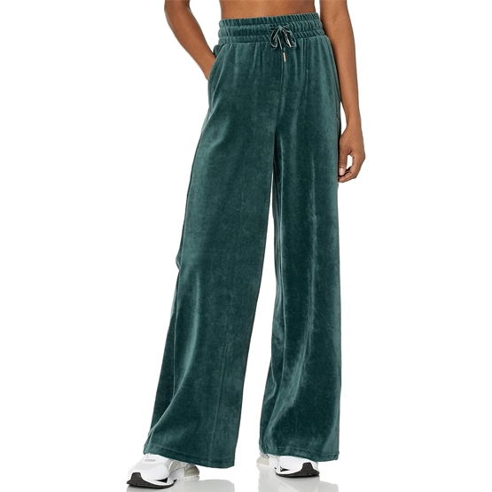 Puma Her Velour Wide Drawstring Pants are teal, wide-legged, and feature an elastic waistband with a drawstring. They offer a relaxed fit with a velvety texture, paired with white sneakers in the image.