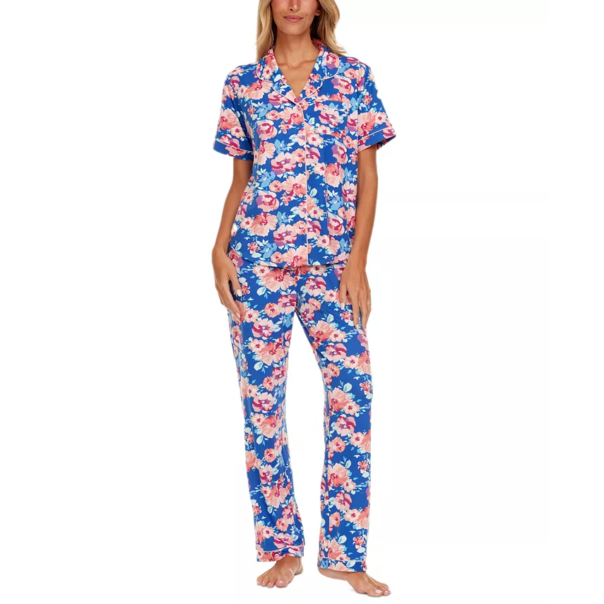 A woman is wearing a two-piece pajama set with a vibrant blue and pink floral print, featuring a short-sleeved button-up top and matching long pants.