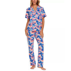 A woman is wearing a two-piece pajama set with a vibrant blue and pink floral print, featuring a short-sleeved button-up top and matching long pants.