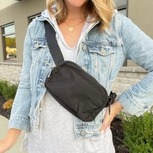 A woman is wearing a light denim jacket, a white top, and a black crossbody bag.