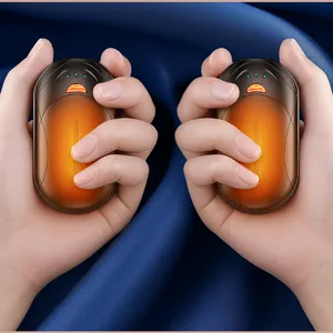 Two hands are holding orange, oval-shaped hand warmers against a blue fabric background.