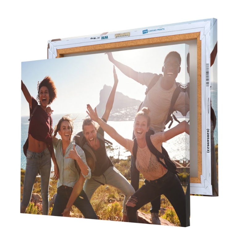 A group photo of friends with backpacks is printed on a canvas, showing a scenic outdoor background with mountains and water, mounted on a wooden frame.