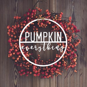 A wreath of red berries on a wooden background with the text \“PUMPKIN everything\“ across the center.