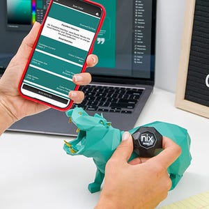 A hand holding a Nix Mini color sensor next to a teal paper rhinoceros, with a smartphone displaying the matching color information.
