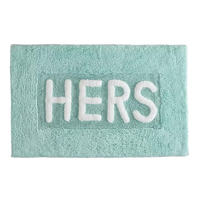 A turquoise bath mat with the word \“HERS\“ in white letters.