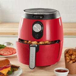A red air fryer with a tray of tater tots is on a kitchen counter, accompanied by a burger, sliced tomatoes, and a cup of ketchup.