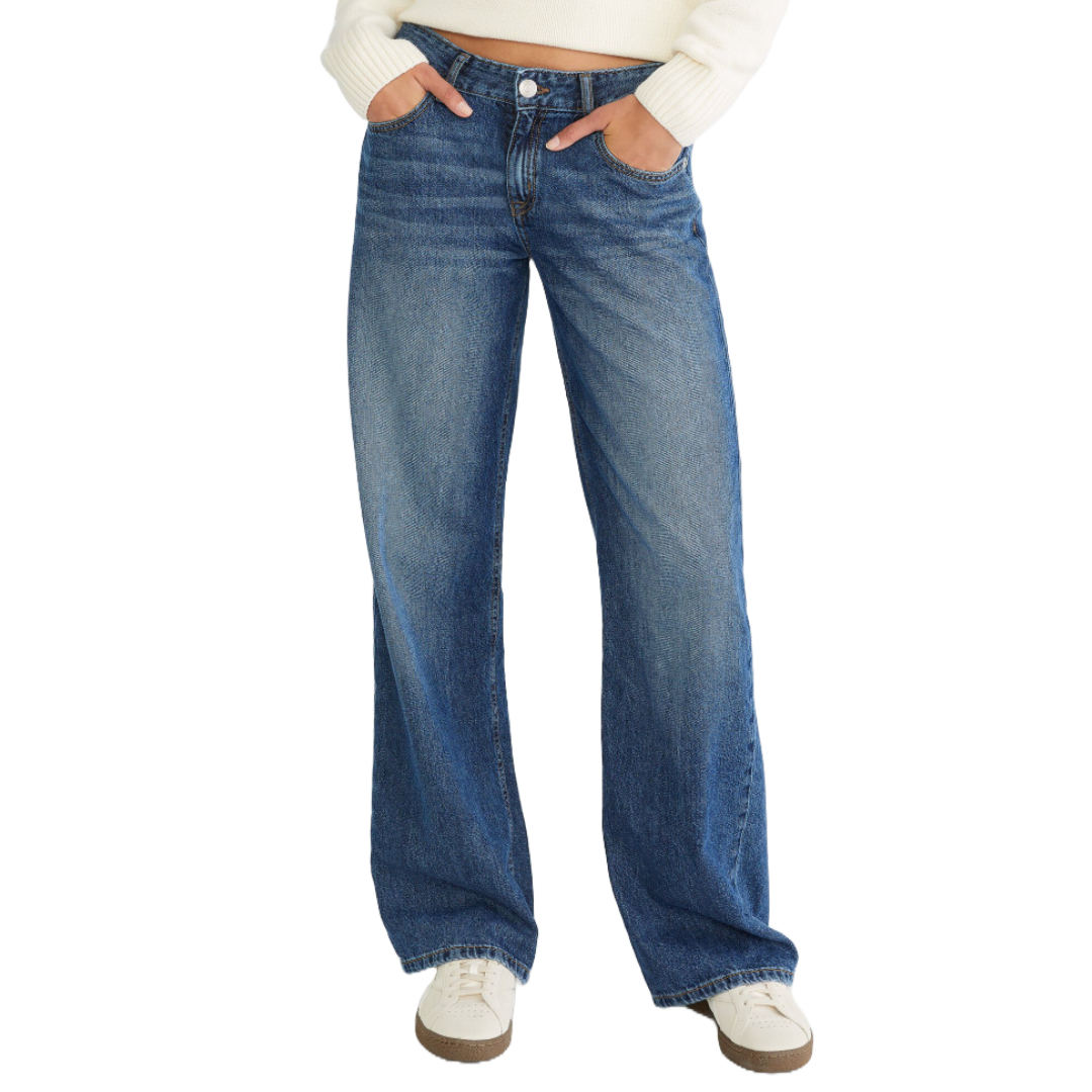 High-waisted baggy jeans made of denim with a button and zipper closure, featuring a faded wash. They have a relaxed fit through the hips and legs, and standard five-pocket styling. Paired with white sneakers and a white sweater.