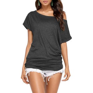 A woman is wearing a dark gray off-the-shoulder T-shirt paired with white distressed denim shorts.