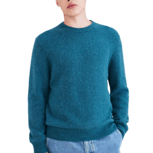 Male model wearing a teal crewneck sweater paired with light blue jeans, hands in pockets.