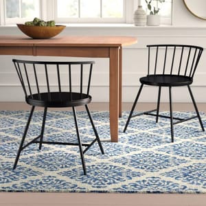 The Laurel Foundry dining chairs are black with a sleek, modern design featuring a curved backrest composed of vertical rods. They have circular seats and angled legs, offering a minimalist and stylish appearance.