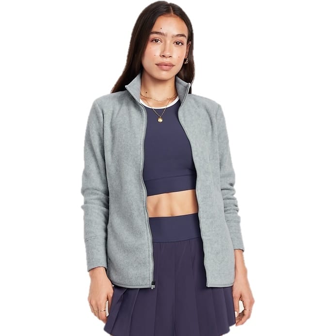 A woman is wearing a light gray, microfleece full-zip jacket with a stand-up collar and long sleeves, paired with a navy sports bra and skirt.