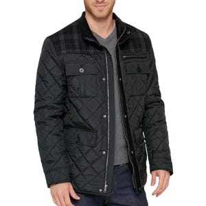 A black quilted jacket with a plaid pattern on the shoulders, featuring multiple pockets with button closures and a zipper front. Modeled with a grey V-neck shirt and dark jeans.