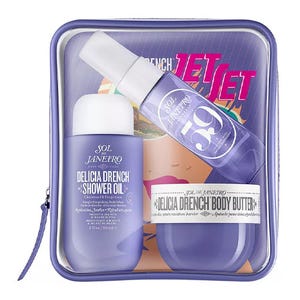 Sol de Janeiro Delicia Drench set includes shower oil, body butter, and spray, all in purple packaging, inside a clear zippered pouch.