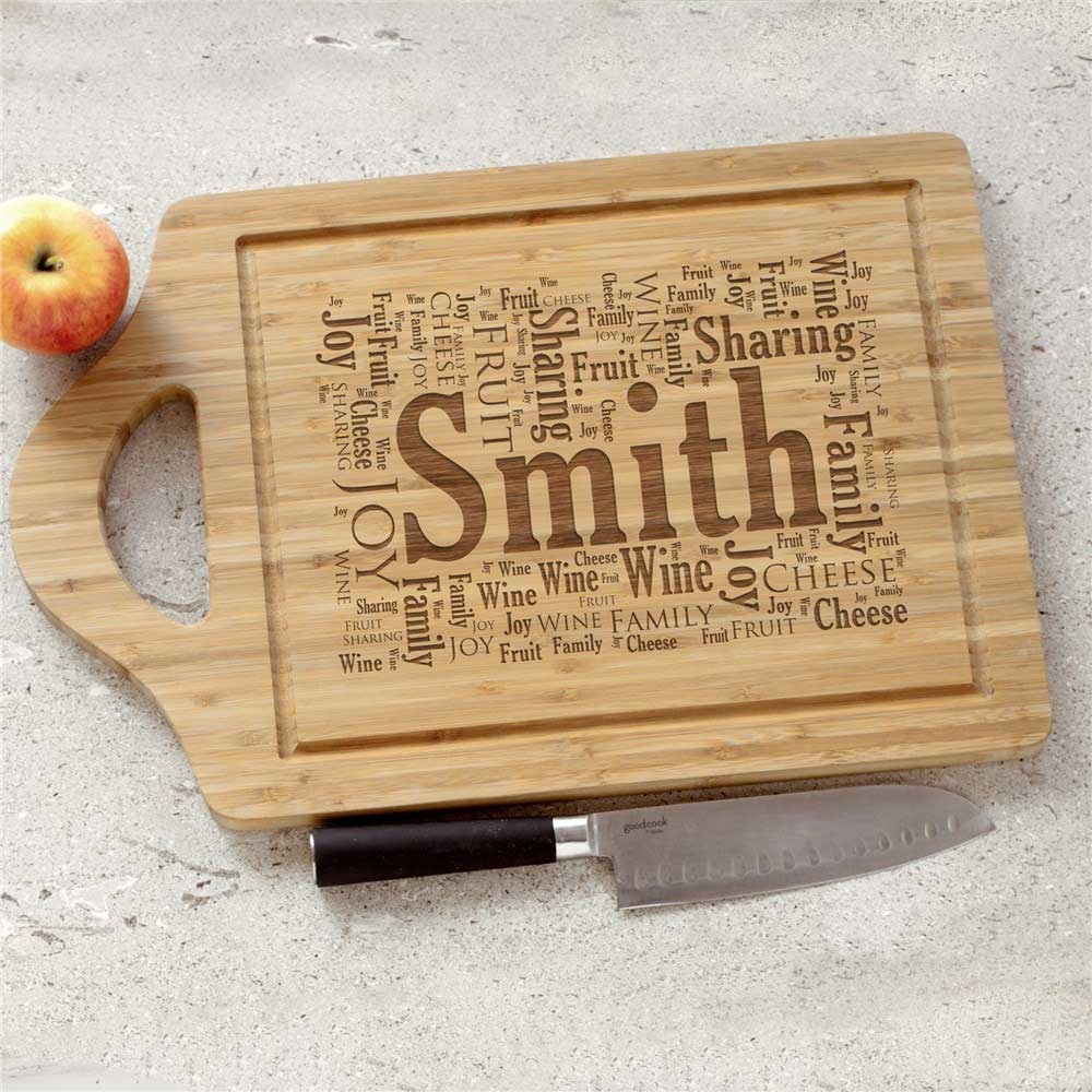 A wooden cutting board with the name \“Smith\“ engraved, surrounded by words like \“Joy,\“ \“Wine,\“ \“Family,\“ \“Fruit,\“ \“Cheese,\“ and \“Sharing.\“ An apple and knife are placed nearby.