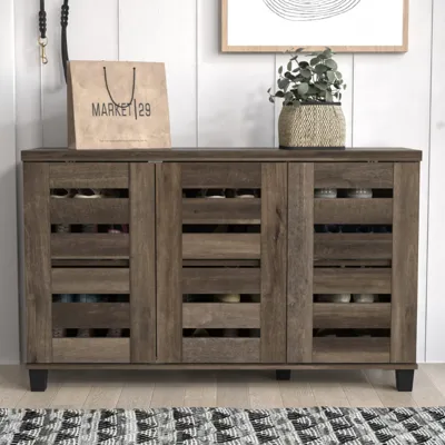 A wooden shoe cabinet with a slatted door design is topped with a paper shopping bag labeled \“Market 29\“ and a potted plant.