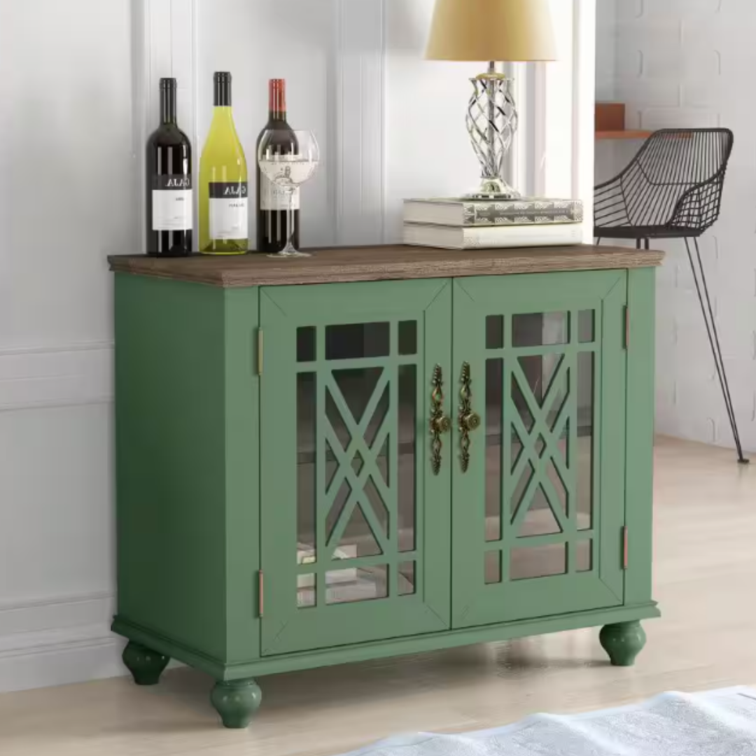 Green sideboard with glass-paneled doors, showcased with three wine bottles, a stack of books, and a table lamp.