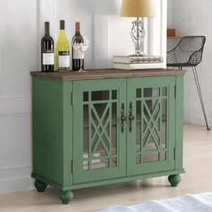 Green sideboard with glass-paneled doors, showcased with three wine bottles, a stack of books, and a table lamp.