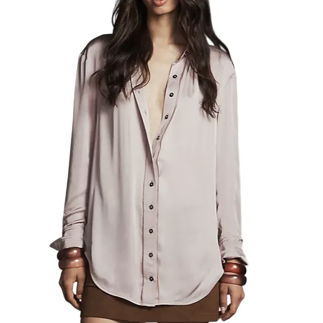 A woman is wearing a light pink blouse with buttons, a short brown skirt, and brown high-heeled boots. She accessorizes with large bracelets on both wrists.