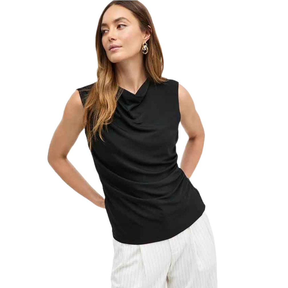 A woman is wearing a black sleeveless draped tank with a gathered neckline, paired with white pinstriped pants. She has long brown hair and is accessorized with gold hoop earrings.