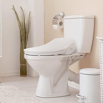 A white toilet with a closed lid next to a small trash can, set against a neutral-toned bathroom wall with a toilet paper holder.
