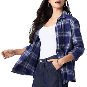 A person wears a blue plaid button-up shirt over a white tank top, paired with dark jeans. The shirt is styled partially open, and the person accessorizes with a bracelet and hoop earrings.
