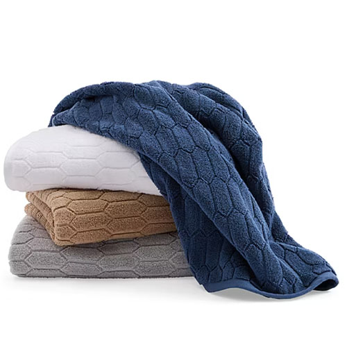 Stack of four textured towels in blue, white, beige, and gray, featuring a hexagonal pattern.