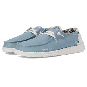 Light blue canvas shoes with lace-up fronts, white soles, and patterned interior, featuring small embroidered details and orange accents on the loops and tags.