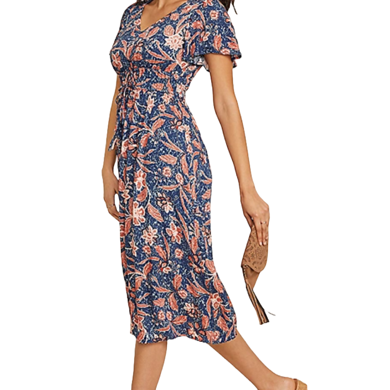 A woman is wearing a blue and orange floral-patterned midi dress with short sleeves and a V-neckline, paired with a beige clutch.