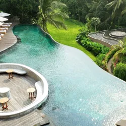 An infinity pool with wooden deck seating features umbrella-shaded loungers and lush greenery, offering a tropical, relaxing atmosphere.