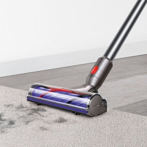 a close up image of a Dyson V8 Plus Cordless Vacuum sucking up debris off of a carpeted floor