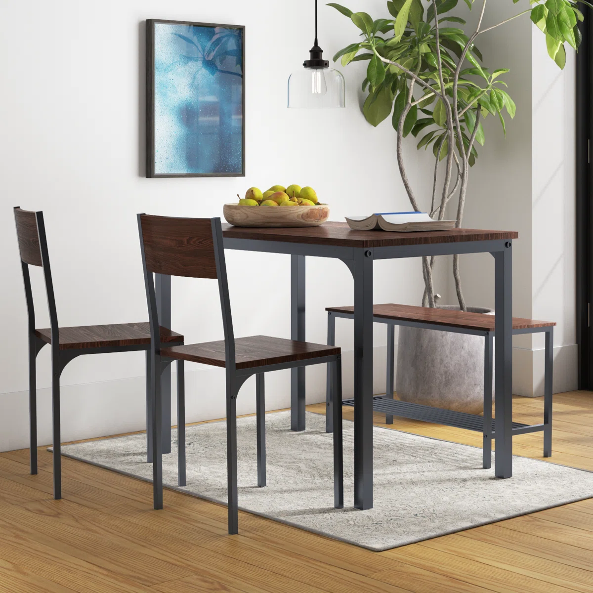 A compact dining set includes a table, two chairs, and one bench, featuring a metal frame with wood surfaces. It's placed on a light rug, accented by a bowl of fruit, a potted plant, and modern art on the wall.