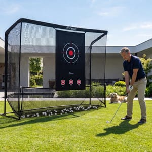A man practices golf in his backyard using an Oxygïe golf practice net with a target. A dog lies nearby on the grass.