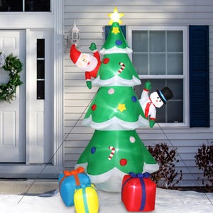 An inflatable outdoor Christmas tree stands at 8 feet tall, featuring a snowman and Santa Claus climbing it, with colorful wrapped gift boxes at its base.