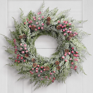 A decorative wreath with snowy greenery, pink berries, and pinecones hangs on a white door next to a lantern-style wall light.