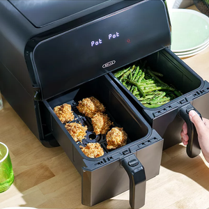 A dual-basket air fryer with breaded chicken in one compartment and green beans in the other.