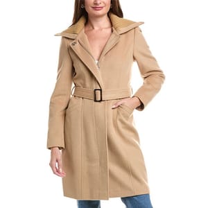 A woman is wearing a beige belted coat with a wide collar, paired with jeans.