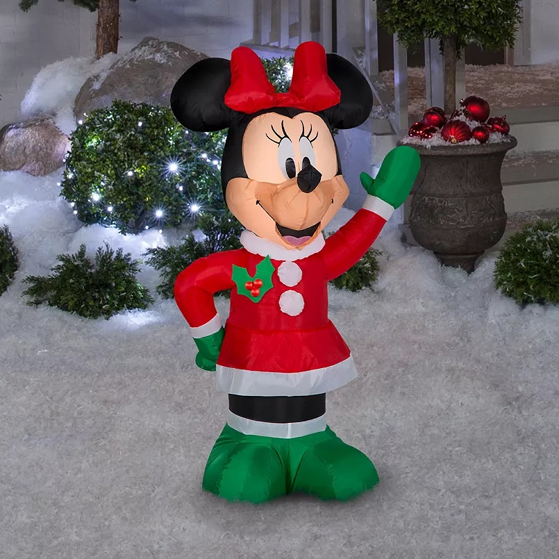 A 3.5ft inflatable Minnie Mouse in a Santa outfit features a red dress, green mittens, and a festive bow, set in a snowy Christmas-themed background with lights and decorations.