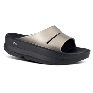 A metallic gold open-toe slide sandal with a thick black sole, featuring a simple design and small circular logo on the side.