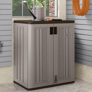 Compact gray storage cabinet with double doors in a garage setting, featuring a watering can on top and coiled hose on the wall.