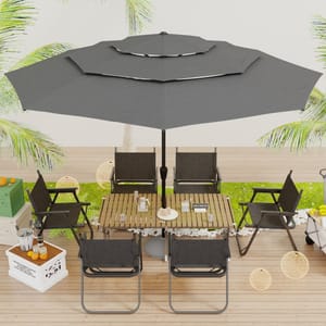 A patio setup featuring a large dark gray umbrella, wooden table, and six matching chairs with metal frames, surrounded by tropical decor and plants, with additional items like a cooler, drinks, and fruit nearby.