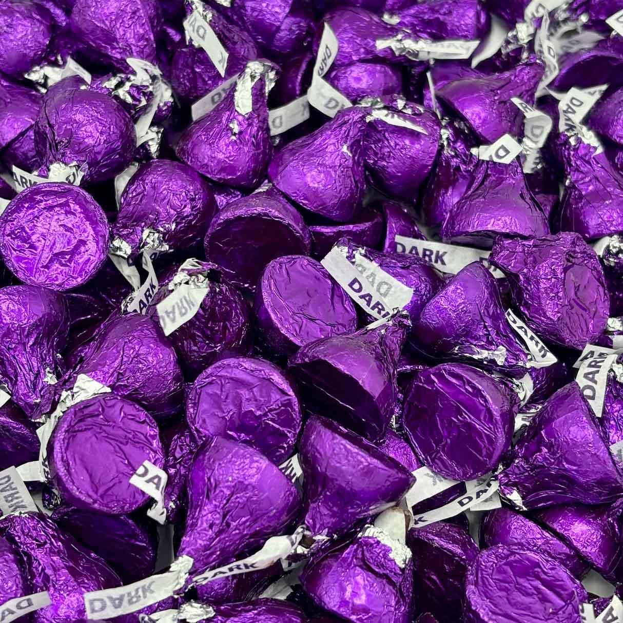 A pile of dark chocolate Hershey's Kisses wrapped in purple foil, each with a paper tag marked \“DARK.\“