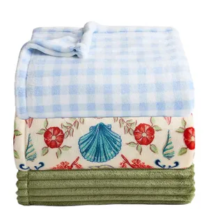 Three folded blankets: a blue and white checkered one, a floral one with seashell and flower patterns, and a plain green one.