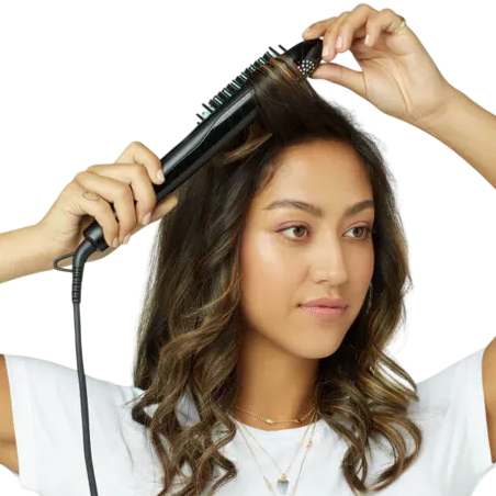 A woman uses a heated straightening brush on her hair, creating smooth, styled curls.