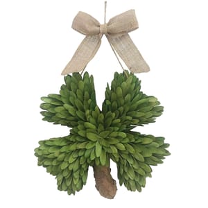 A shamrock wreath made of green leaves arranged to form a three-leaf clover shape, accented with a brown stem and a burlap ribbon tied in a bow at the top for hanging.