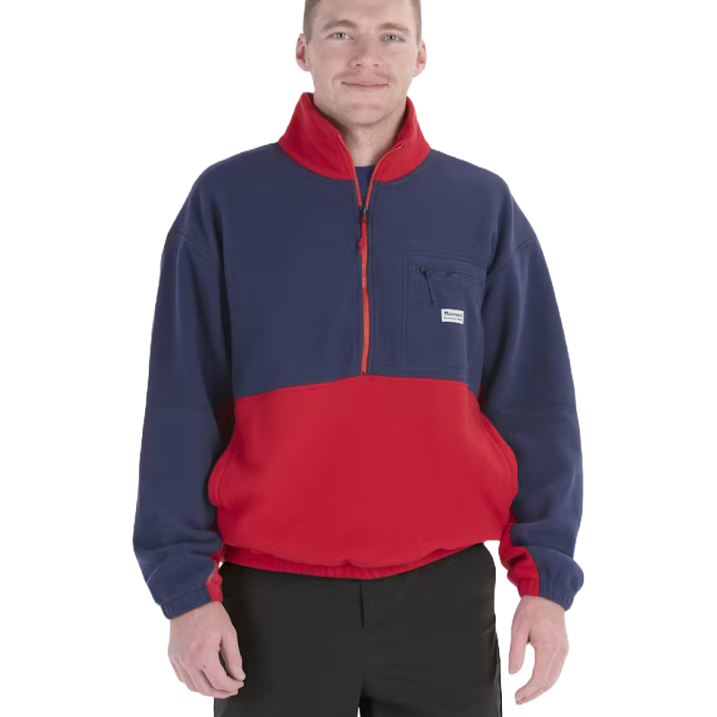 A man wears a color-blocked half-zip fleece pullover with navy and red sections, featuring a chest pocket with a label, paired with black pants.