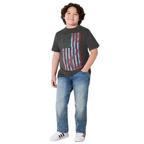A young boy is wearing a dark gray T-shirt with an American flag design, blue jeans, and white Adidas sneakers with black stripes.