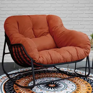 Iron Outdoor Rocker with Cushion features a sturdy black metal frame and a plush, rust-colored cushion, set on a patterned circular rug against a white brick wall. Ideal for outdoor relaxation.