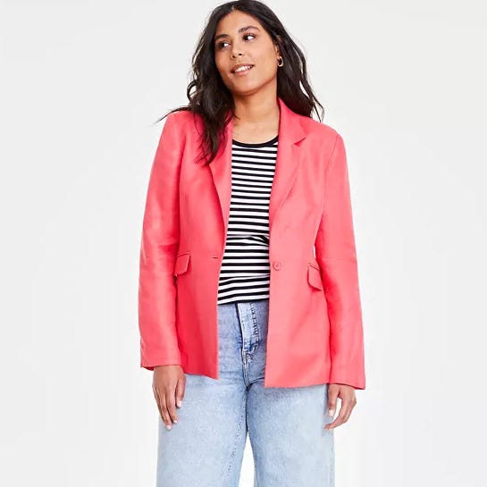 A woman is wearing a coral blazer over a striped top, paired with light blue jeans.